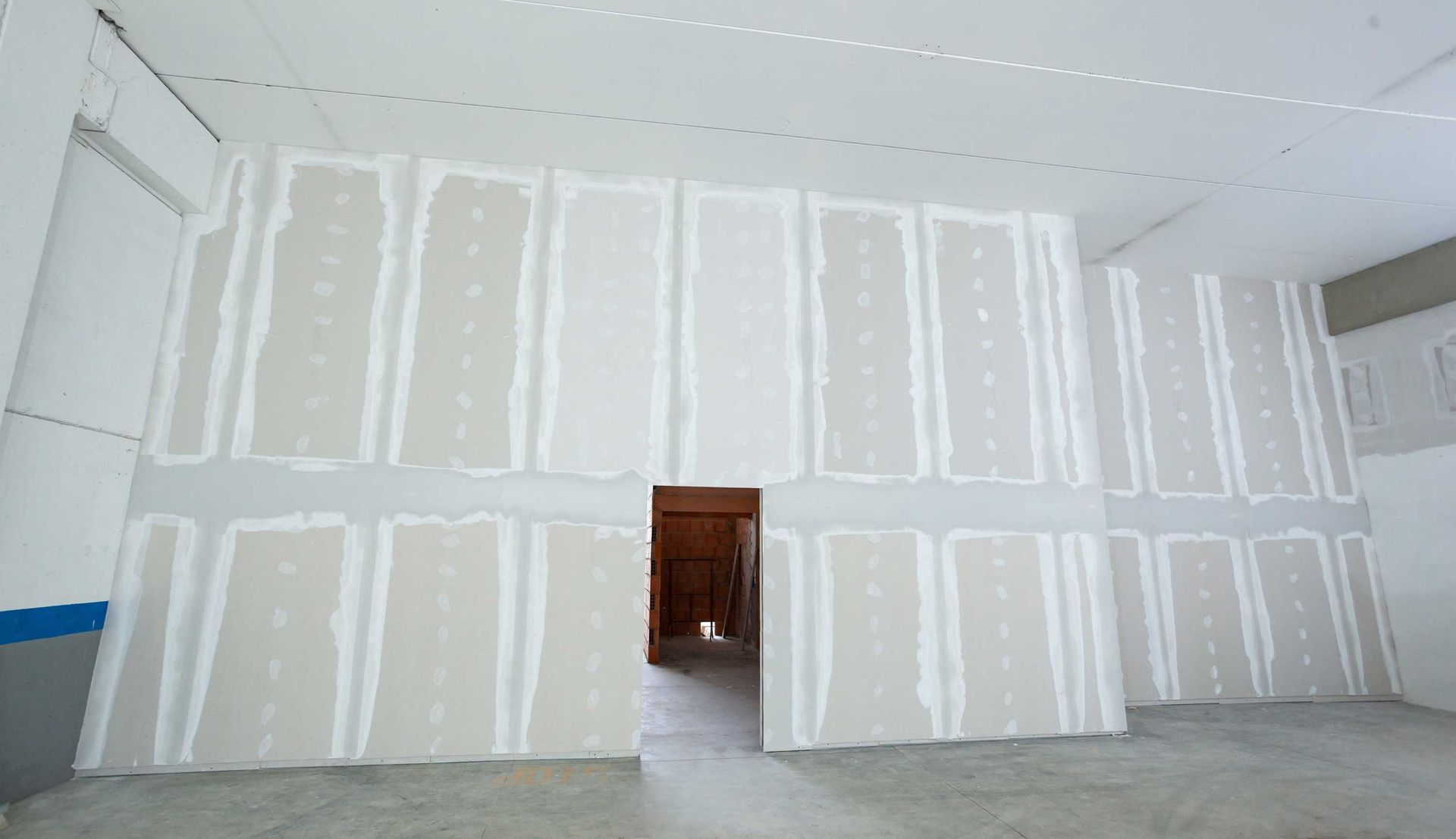 Unfinished room with white drywall, gray floor, and an open doorway with exposed wood.