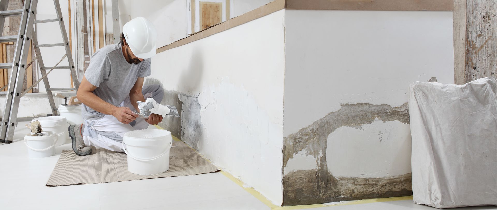 Worker plastering a wall with white paint in a room under construction