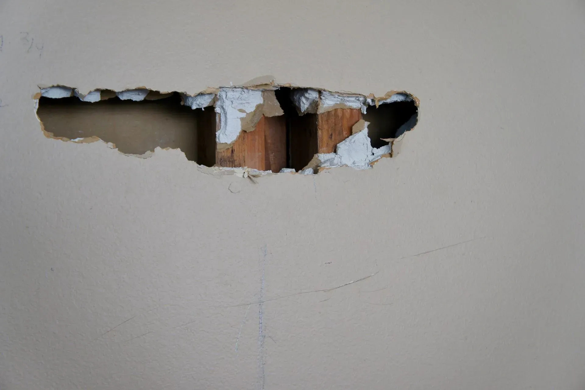 Hole in a beige wall exposing damaged drywall and wooden studs