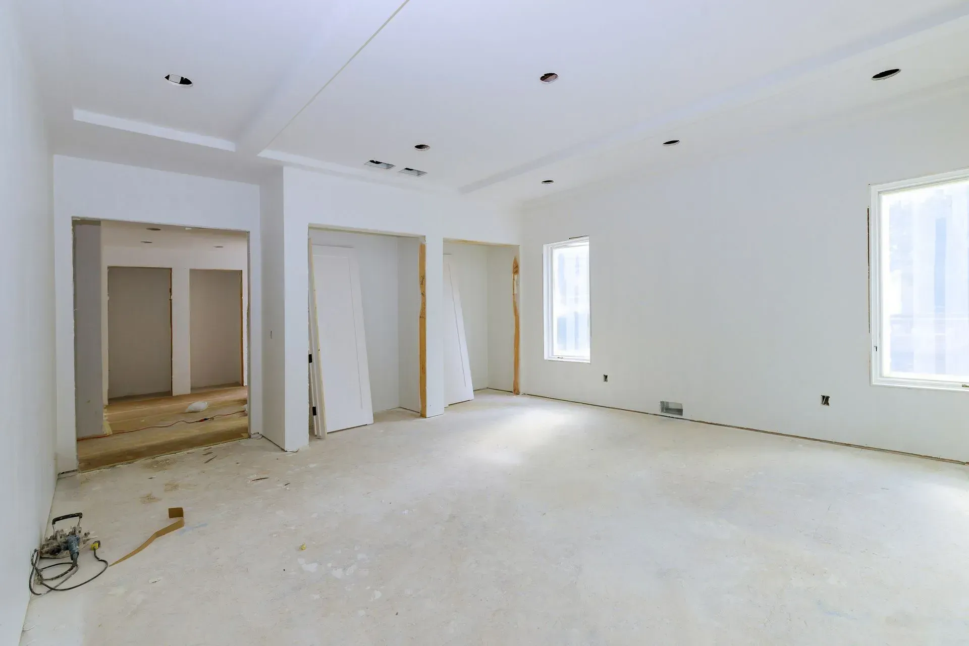 Empty unfinished white room with bare walls, open doorways, and sunlight from two windows