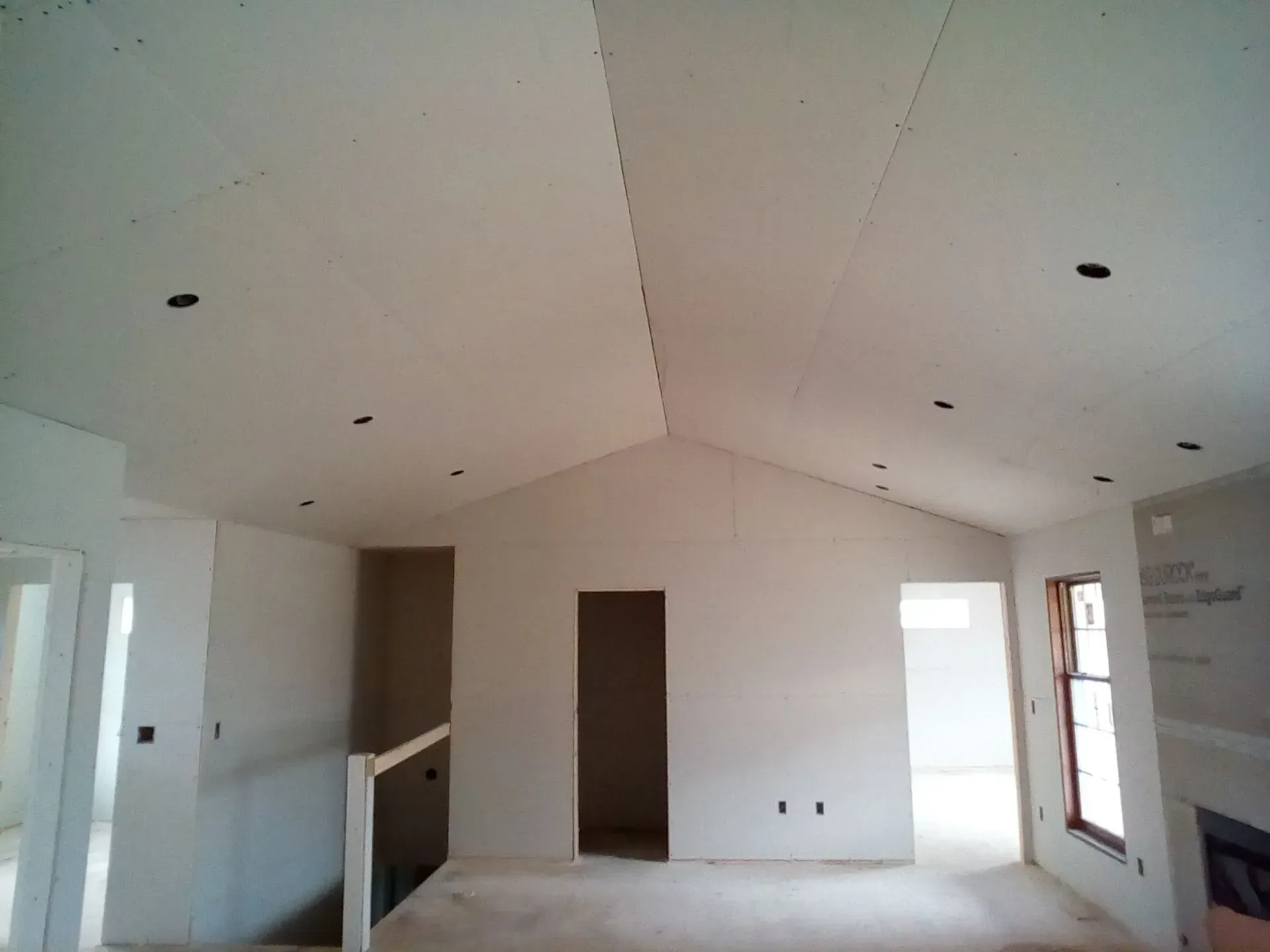 Empty white room with vaulted ceiling, recessed lights, and windows under construction