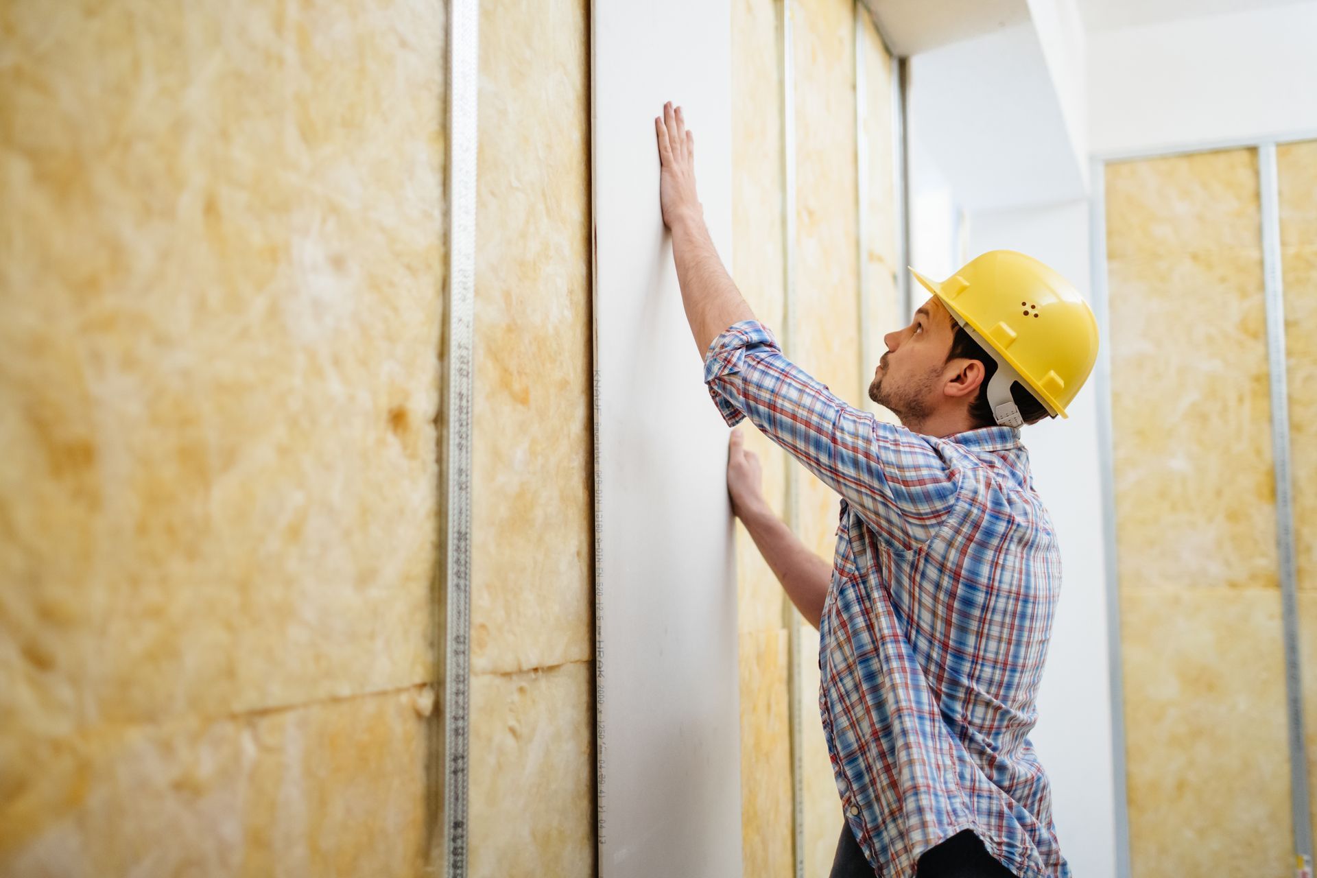 Worker in yellow hard hat installing insulation panels on a wall