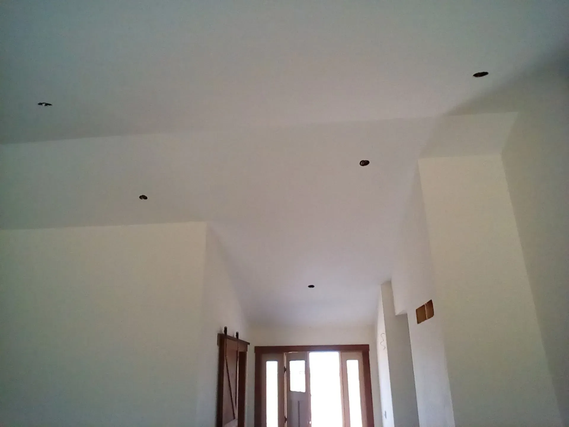 White hallway ceiling with recessed lights and a window at the far end