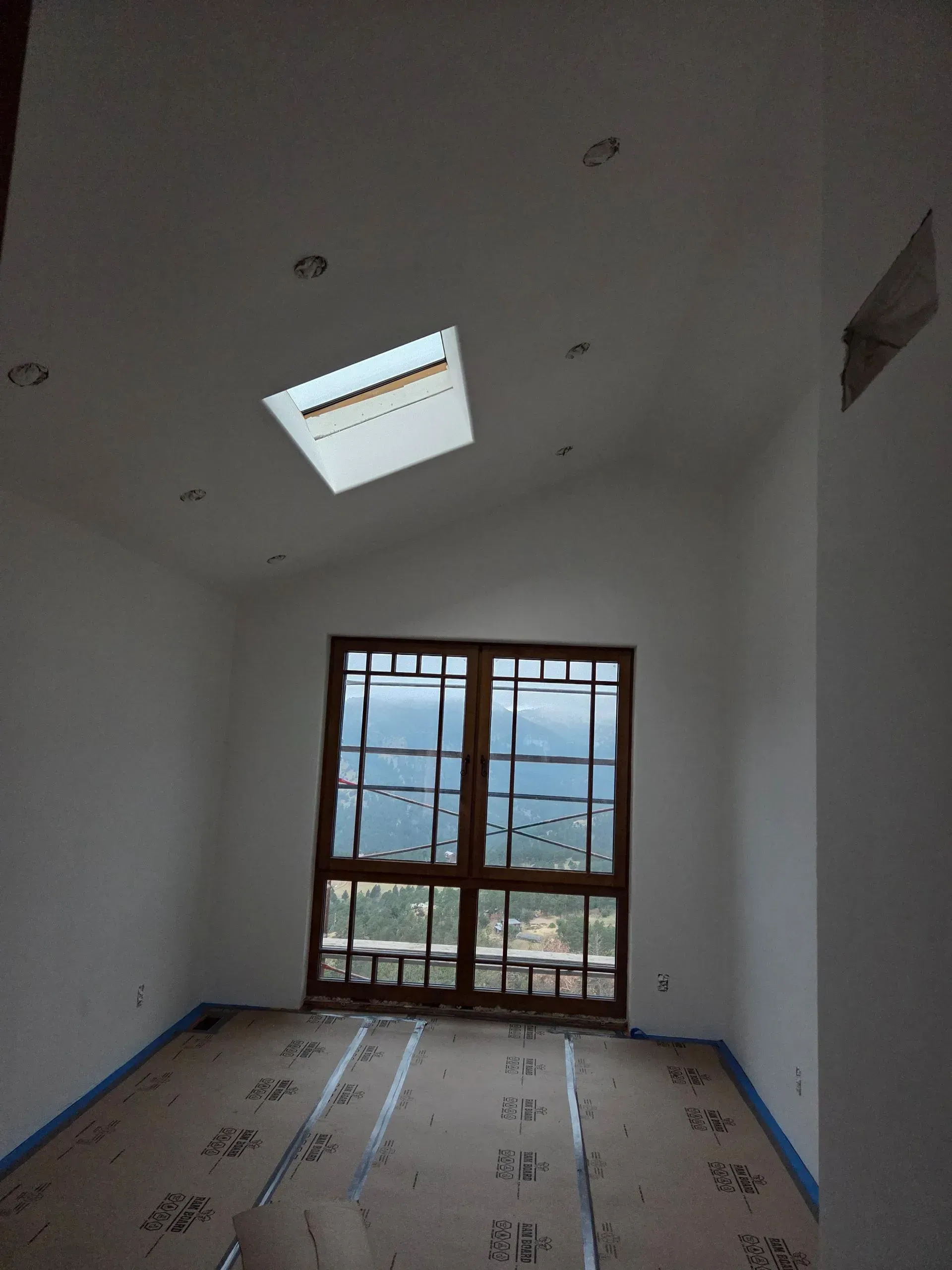 Empty white room with skylight, large window, and covered floor under construction