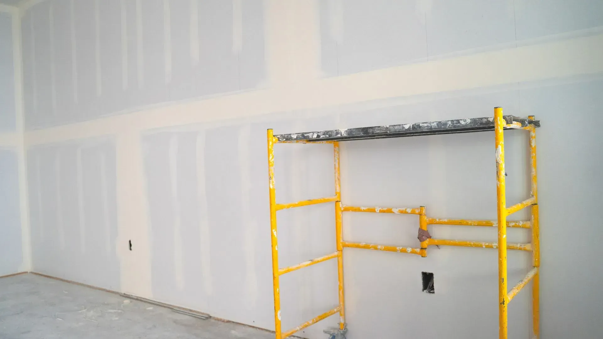 Yellow scaffolding in front of a drywall wall in an unfinished room
