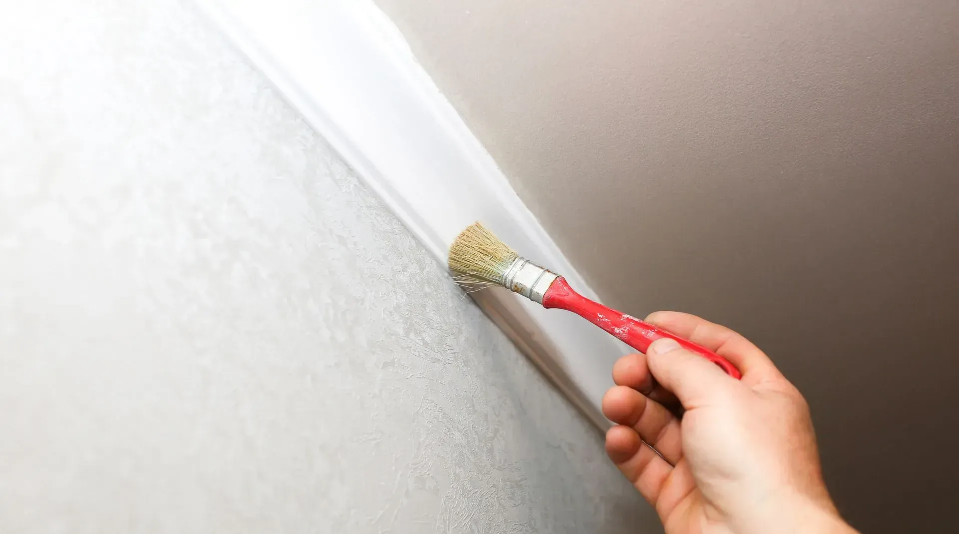 Hand painting a white wall near the ceiling with a red-handled brush