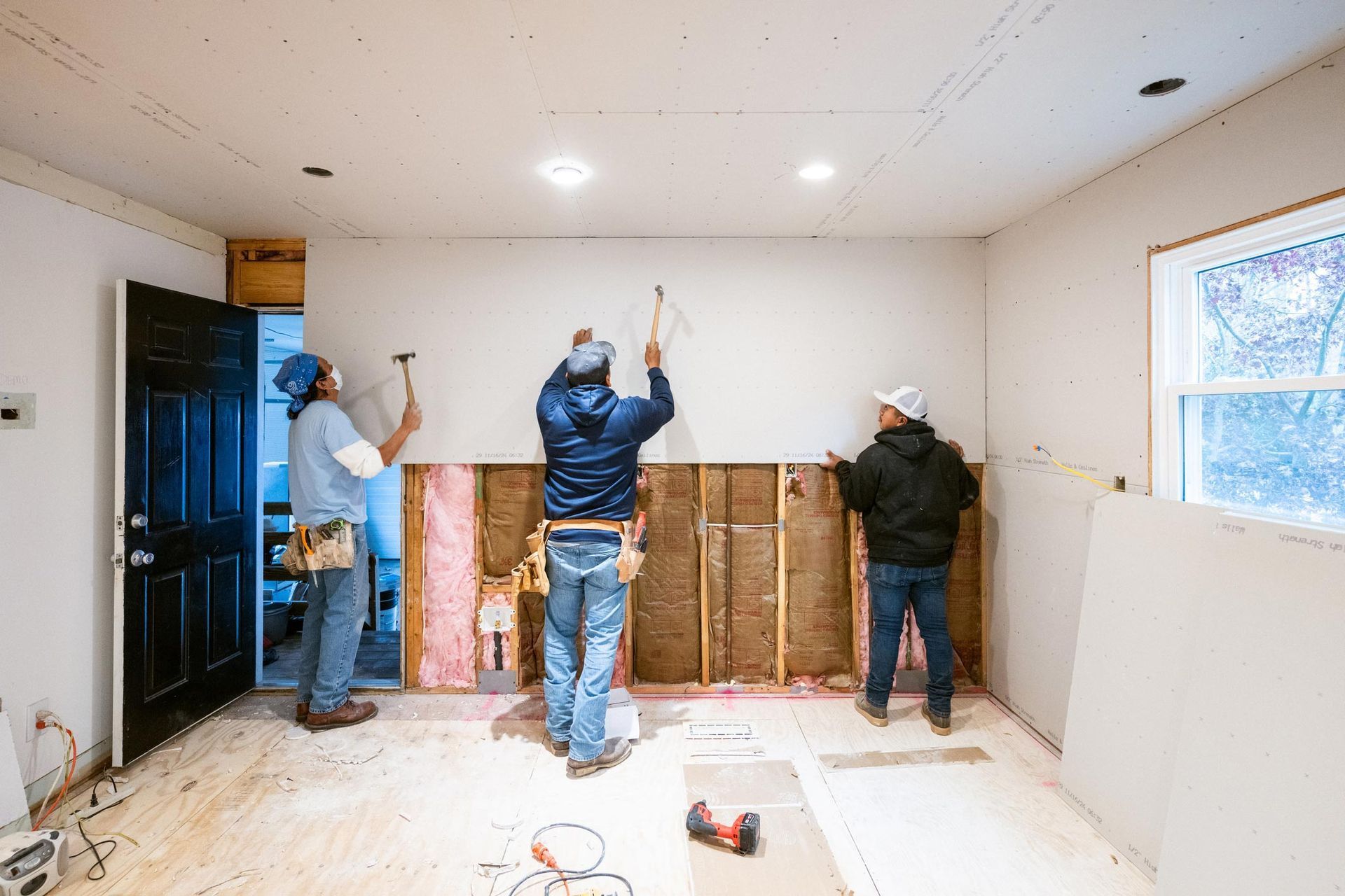 Three workers demolishing wall paneling in a room under renovation