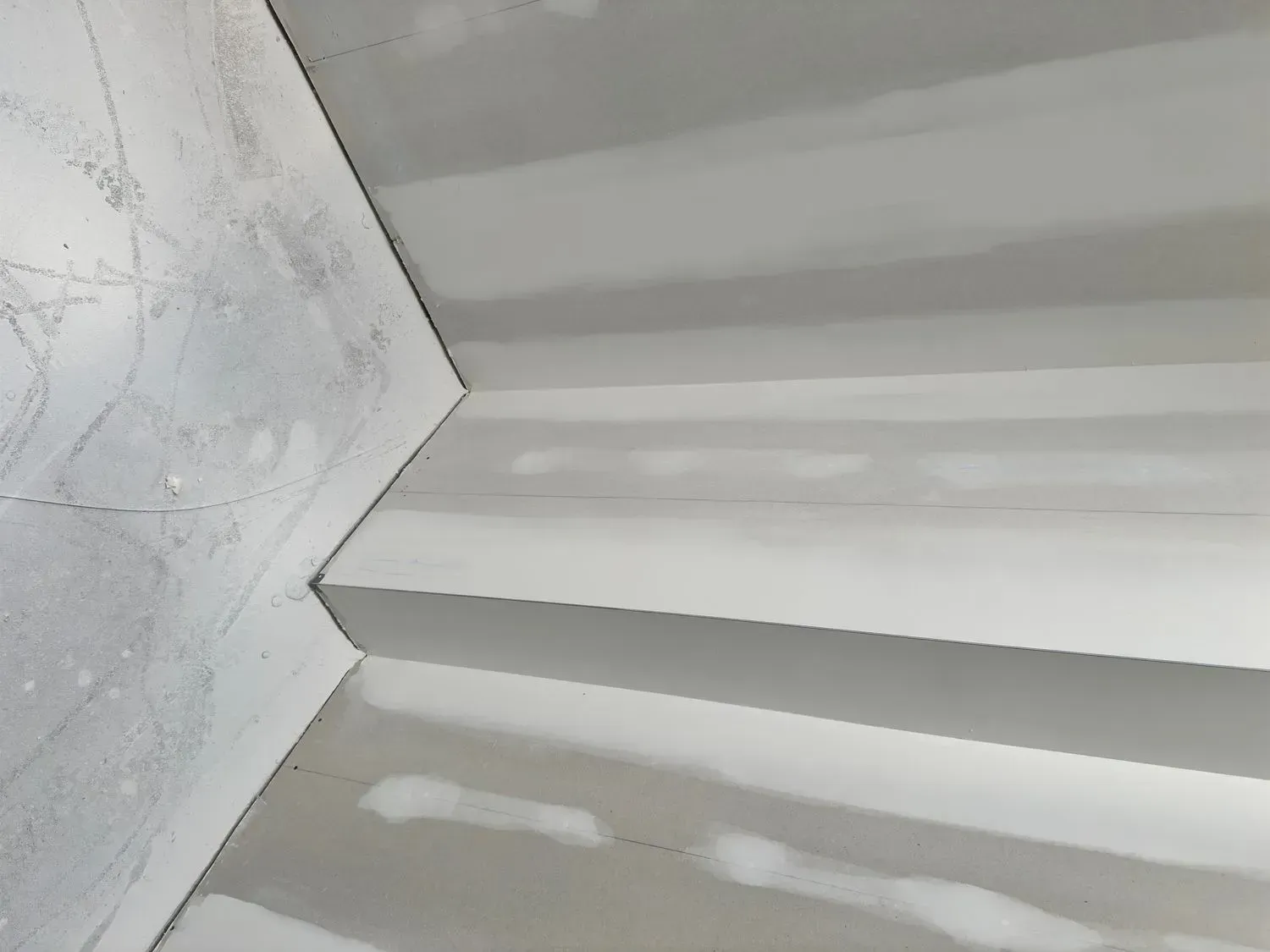 White corrugated ceiling panel beside a textured wall, shown in close-up with soft shadows.
