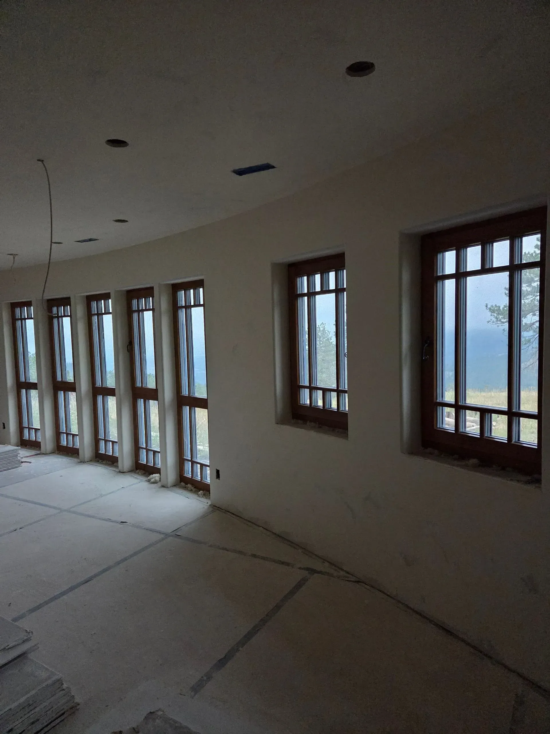 Empty room under construction with white walls, unfinished floor, and several windows along one side