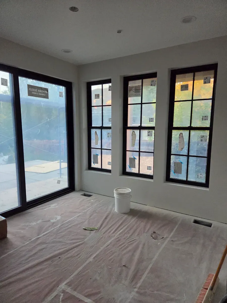 Empty room with plastic-covered floor, black-framed windows, and a glass door letting in daylight