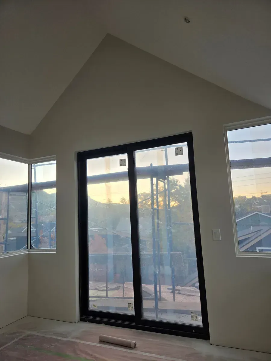 Empty room with sloped ceiling, black sliding glass door, and side windows at sunset.