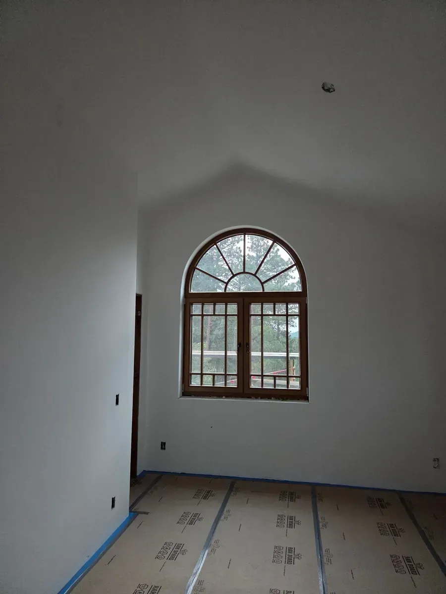 Empty white room with arched window and tiled floor, blue painter’s tape along the baseboards