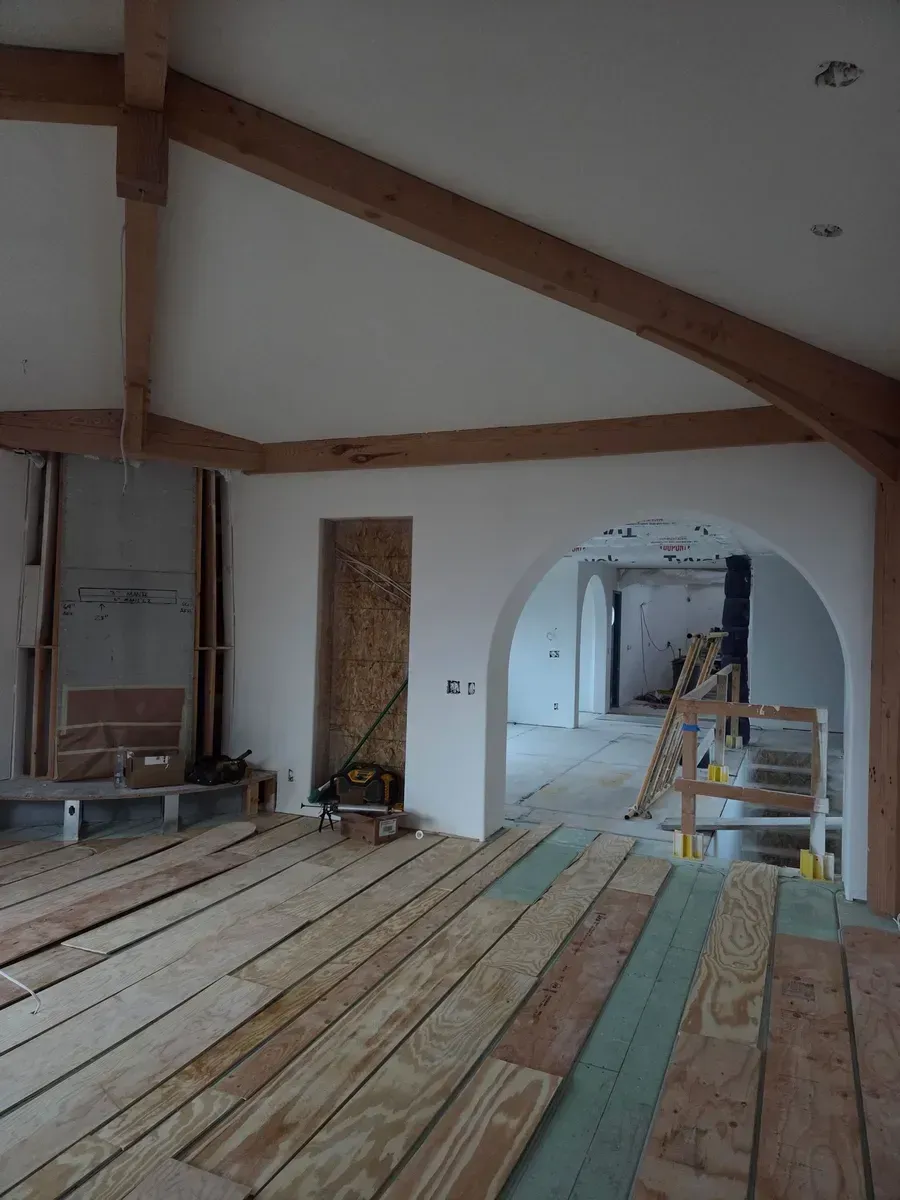 Unfinished room with exposed wooden beams, plank flooring, and a ladder in the doorway.