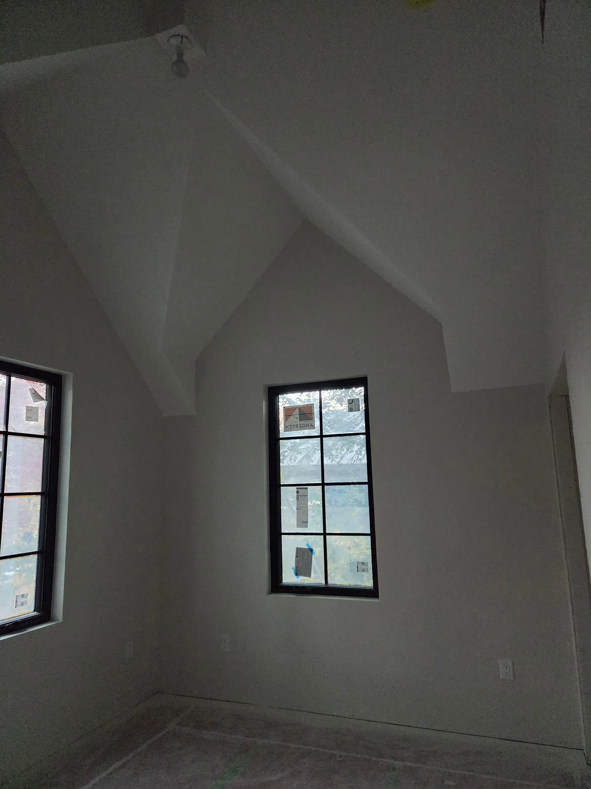 Empty white room with two small windows and a high, sloped ceiling.