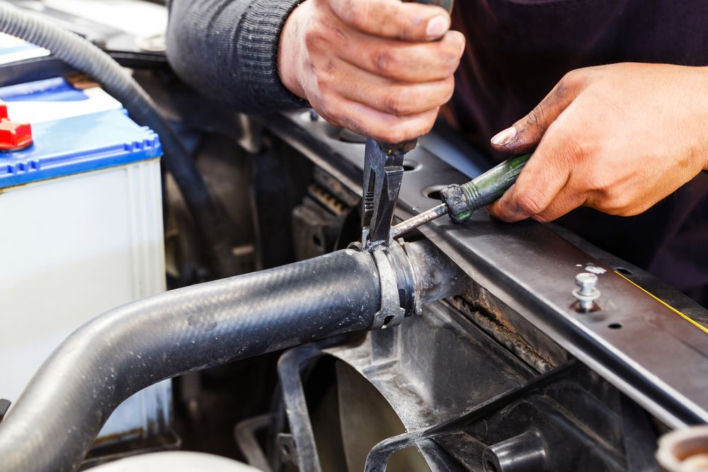 Mechanic using pliers to remove a clamp from a radiator hose in an engine bay
