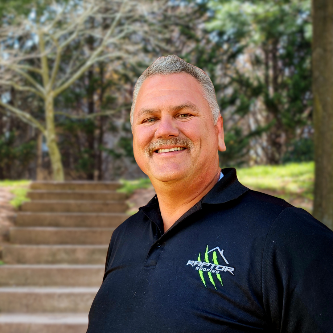 Smiling man in a black polo shirt, outdoors near stone steps.