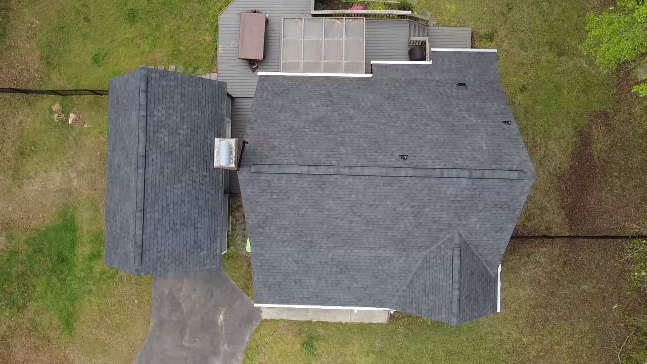 Aerial view of a house with a dark gray roof, surrounded by green grass and a driveway.
