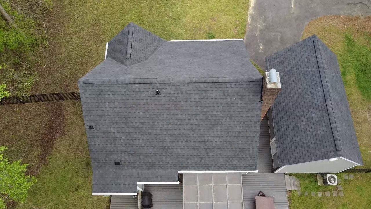Overhead view of a house with dark gray roof, chimney, and a driveway surrounded by greenery.