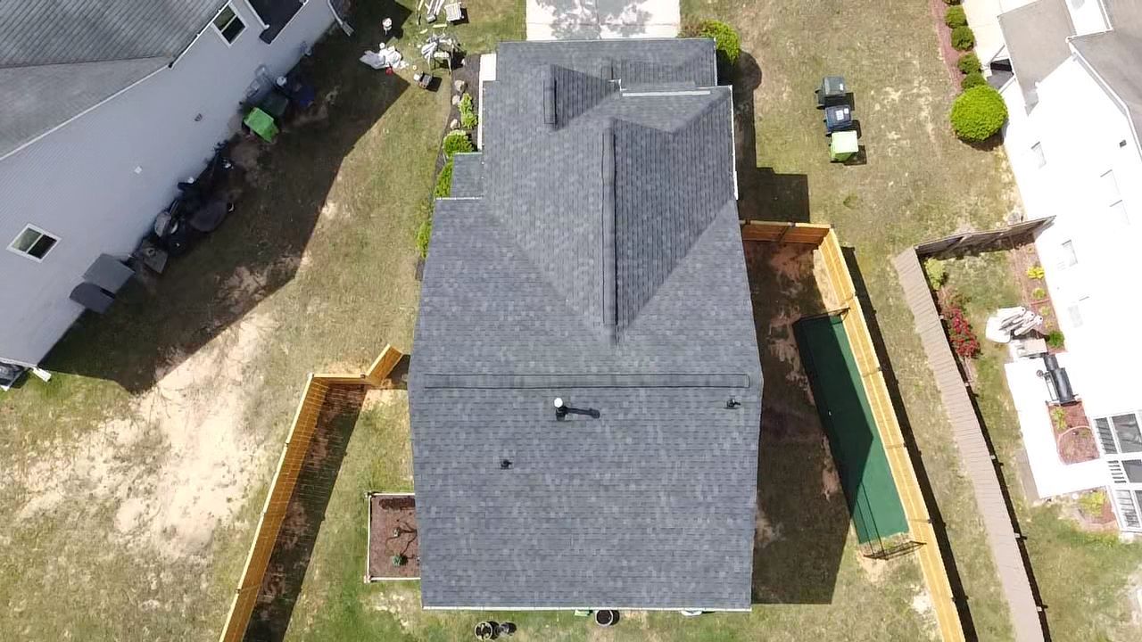 Overhead view of a house with a gray roof, surrounded by a tan fence and green grass.