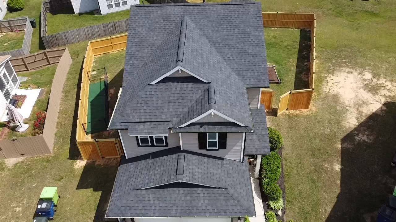Overhead view of a two-story house with a gray roof and a wooden fence in a yard.