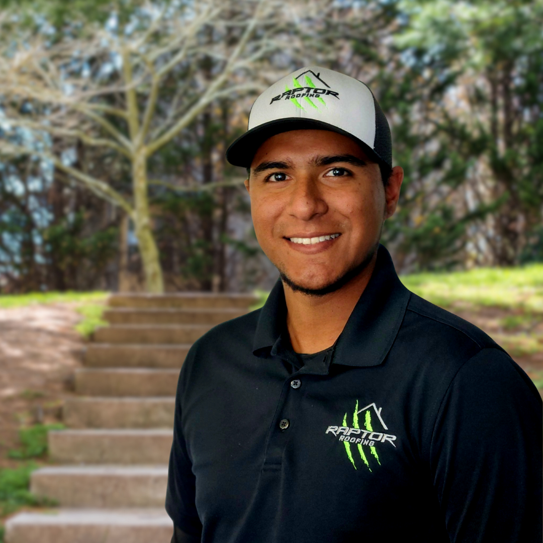Man smiling, wearing a black polo shirt and hat with green logo; steps and trees in the background.