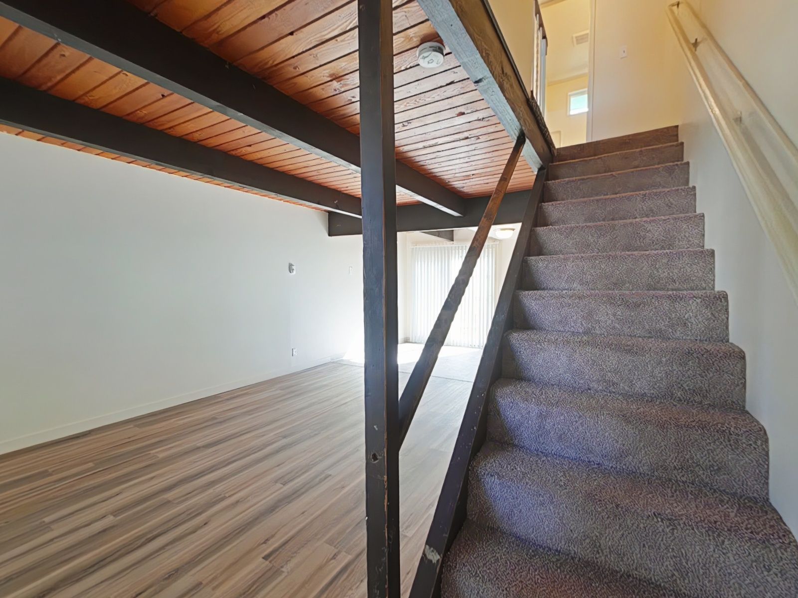 Remodeled living room with laminated flooring, refinished handrail and clean carpeted stairs.