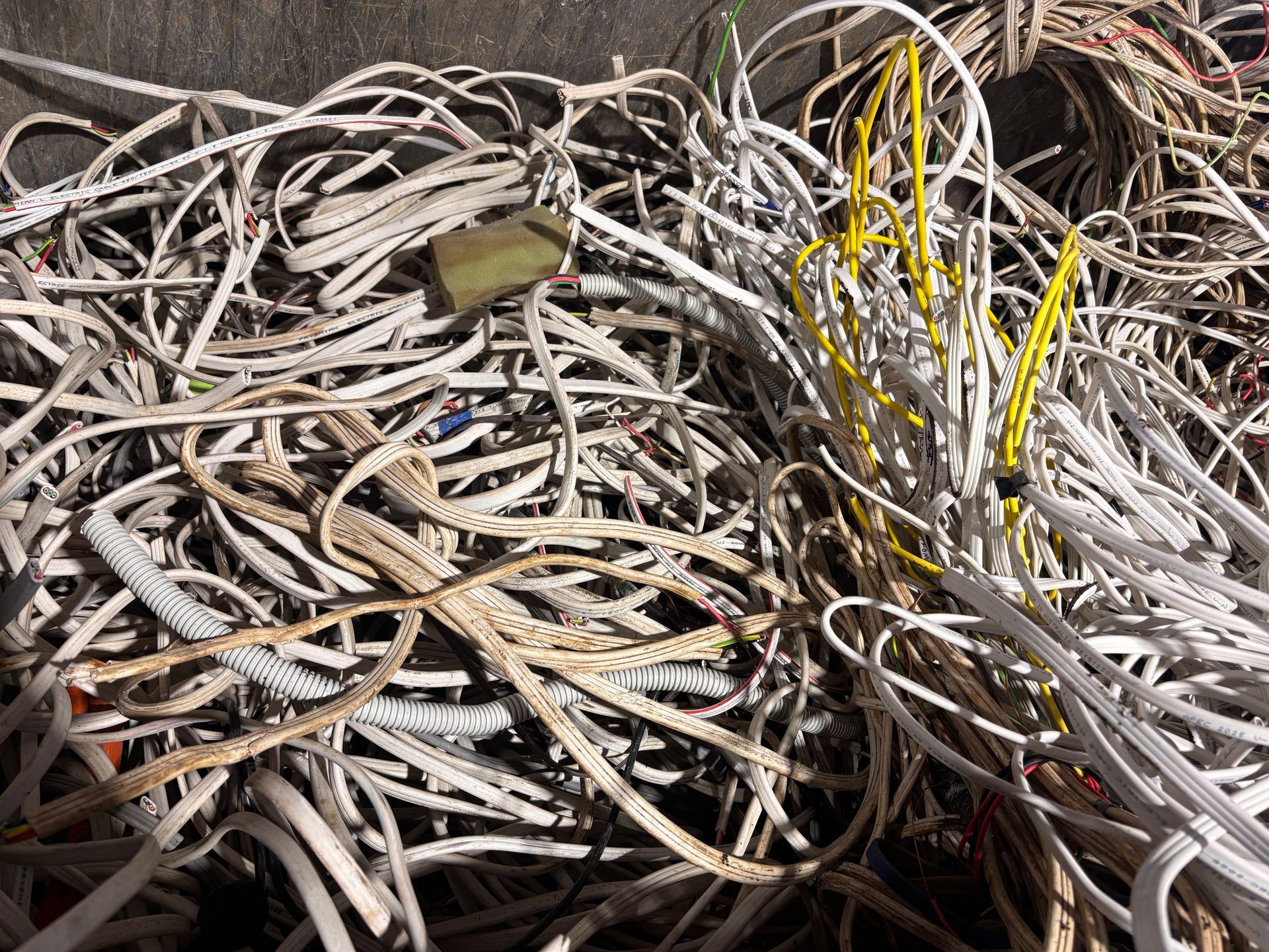 Tangled pile of white, beige, and yellow electrical wires, some with a flattened, tape-like appearance— Independent Scrap Metal Pty Ltd in South Lismore, NSW