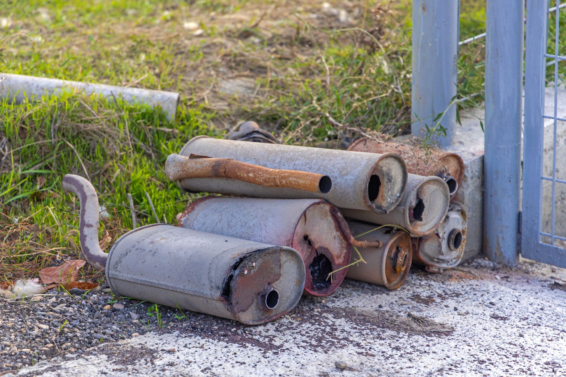 Pile of Discarded Rusty Car Mufflers Next to a Metal Gate and Grassy Area — Independent Scrap Metal Pty Ltd in Ballina, NSW