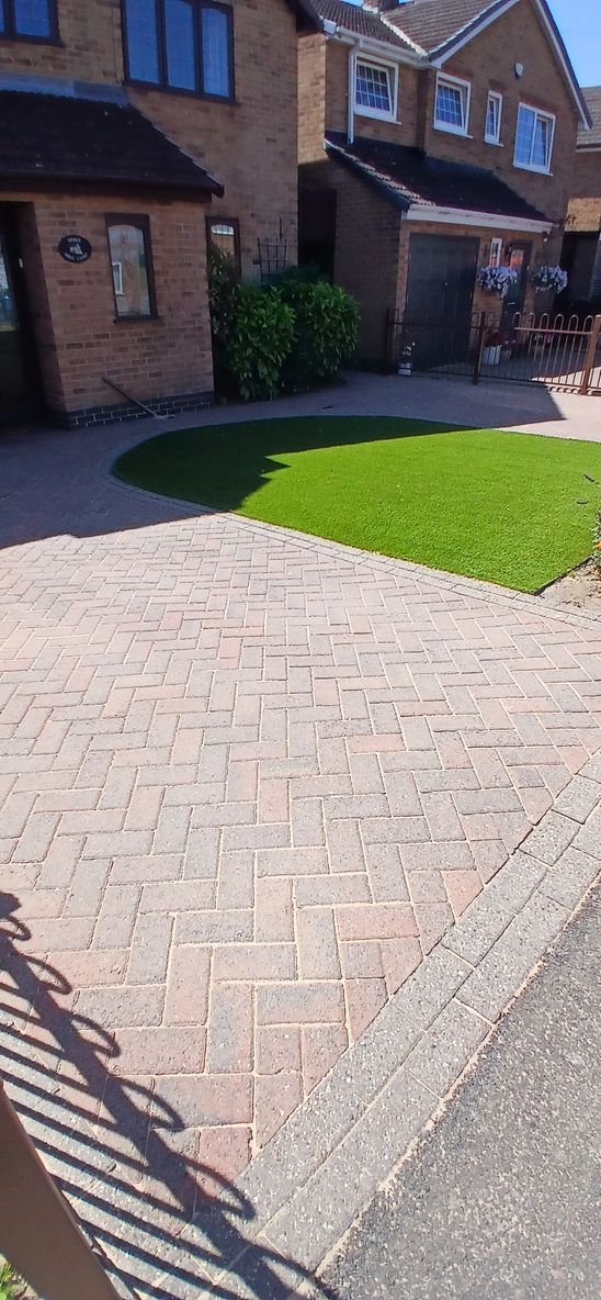A block paved driveway in front of a brick house before being pressure washed by benchmark property services.