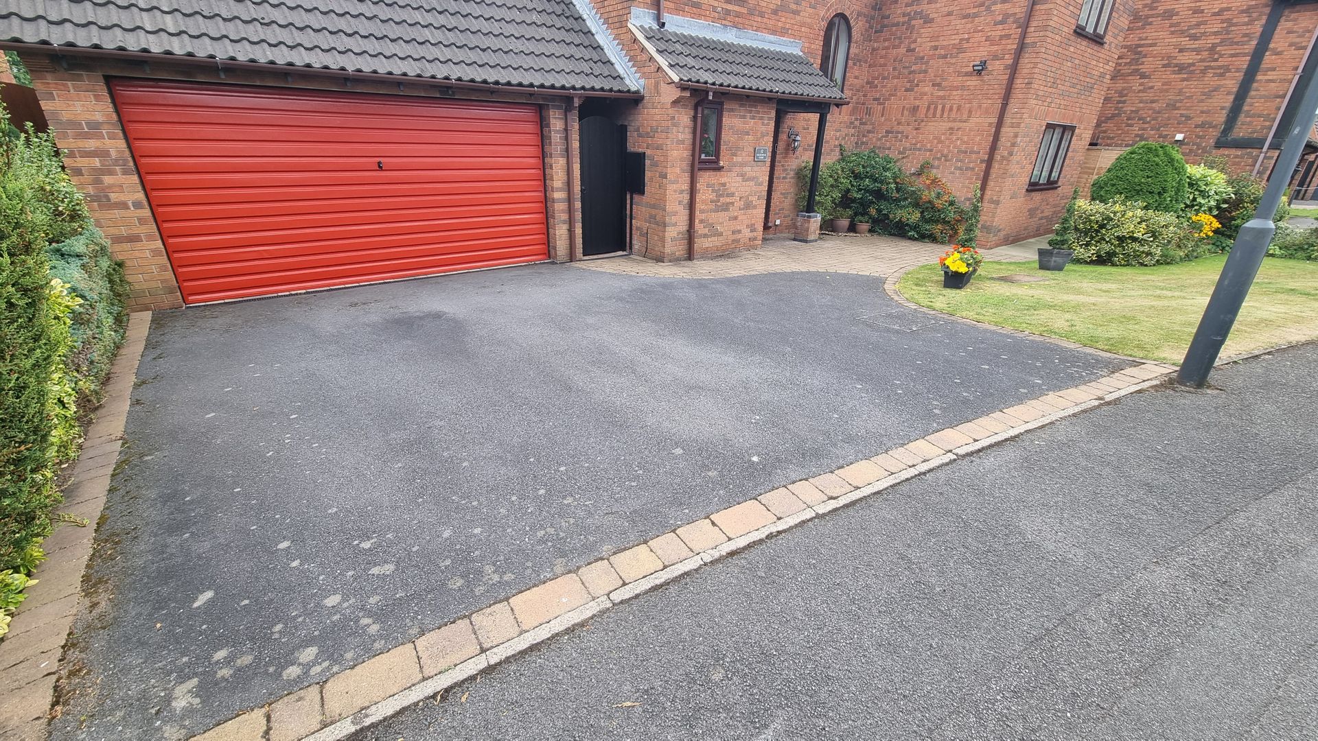 A driveway with a red garage door in front of a brick house.