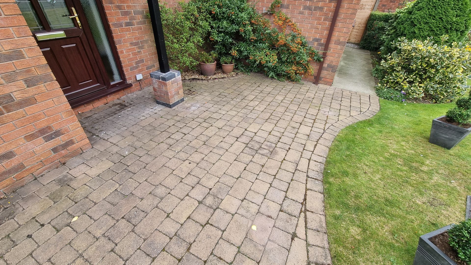 A block paved driveway before being cleaned, leading to the front door of a house.