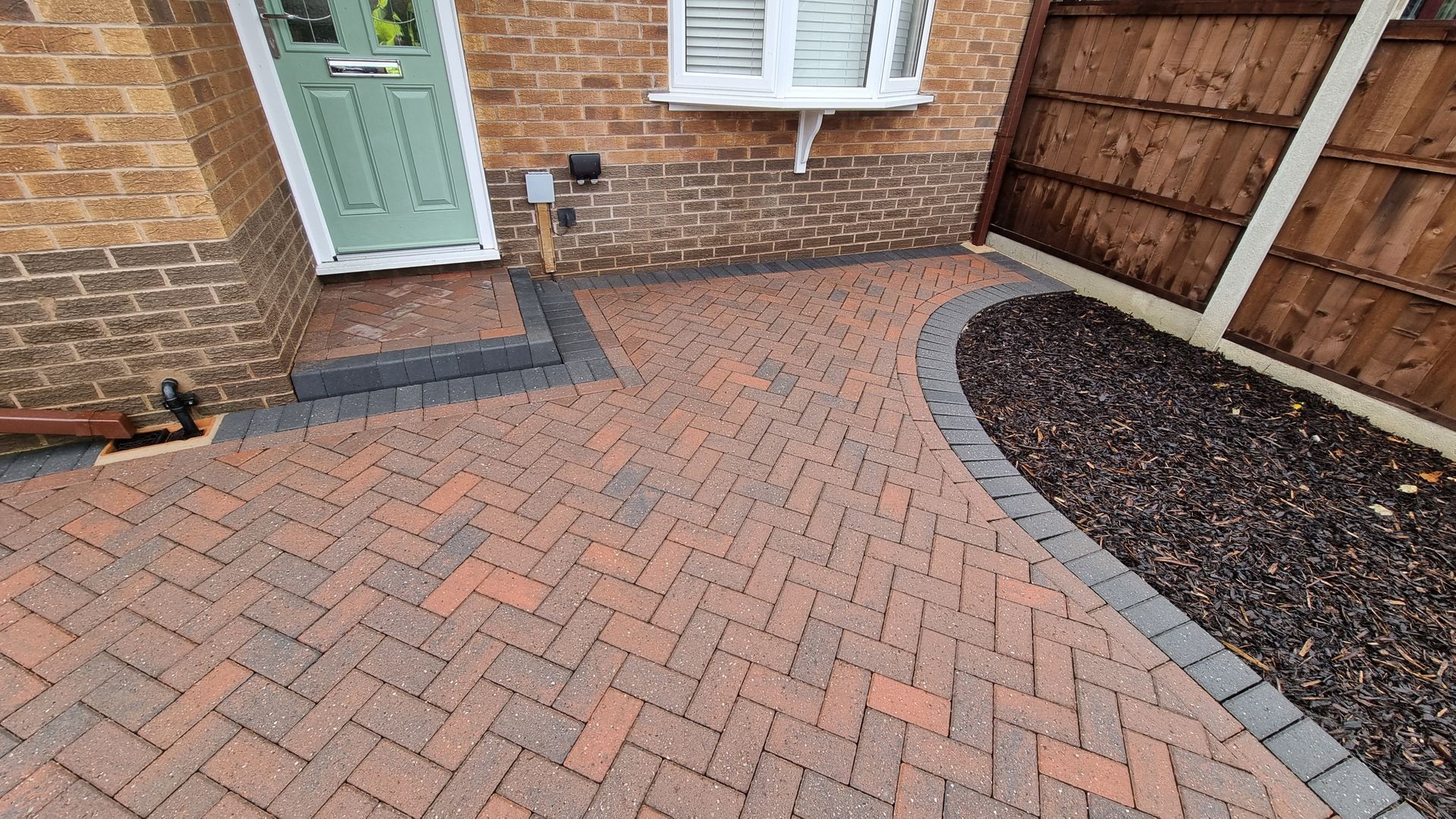 A block paved driveway in front of a brick house before being pressure washed by benchmark property services.