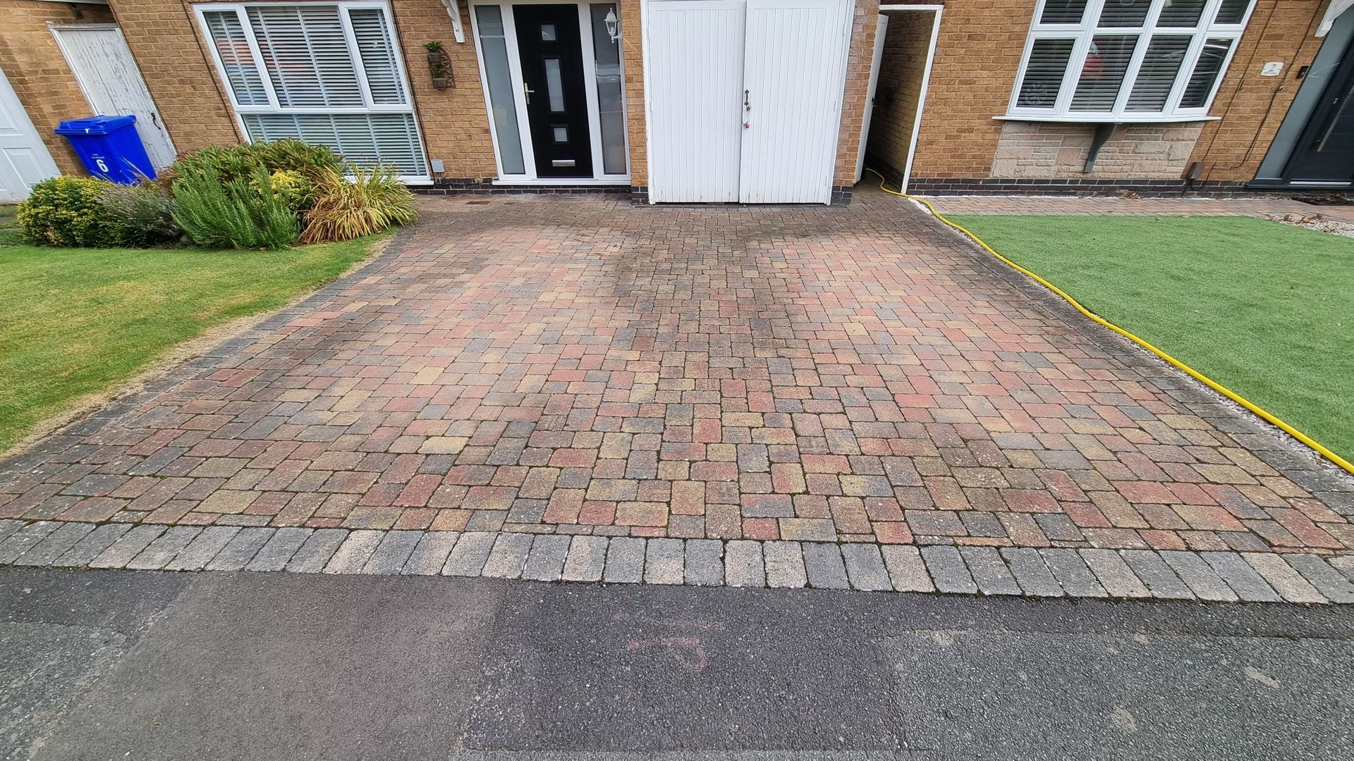 A block paved driveway in front of a brick house before being pressure washed by benchmark property services.