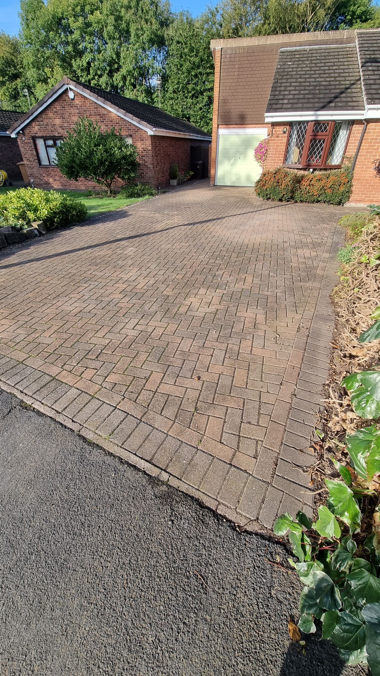 A block paved driveway in front of a brick house after being pressure washed by benchmark property services.