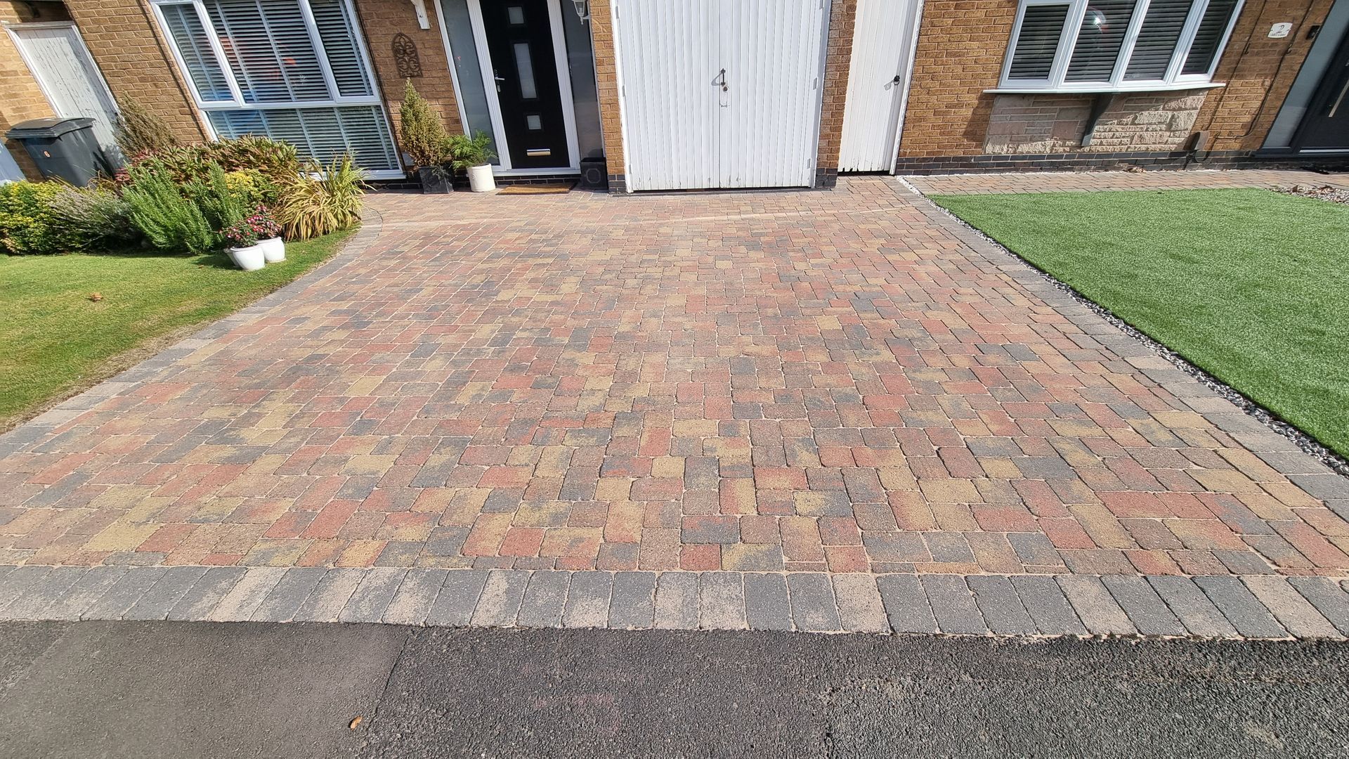 A block paved driveway in front of a brick house after being pressure washed by benchmark property services.