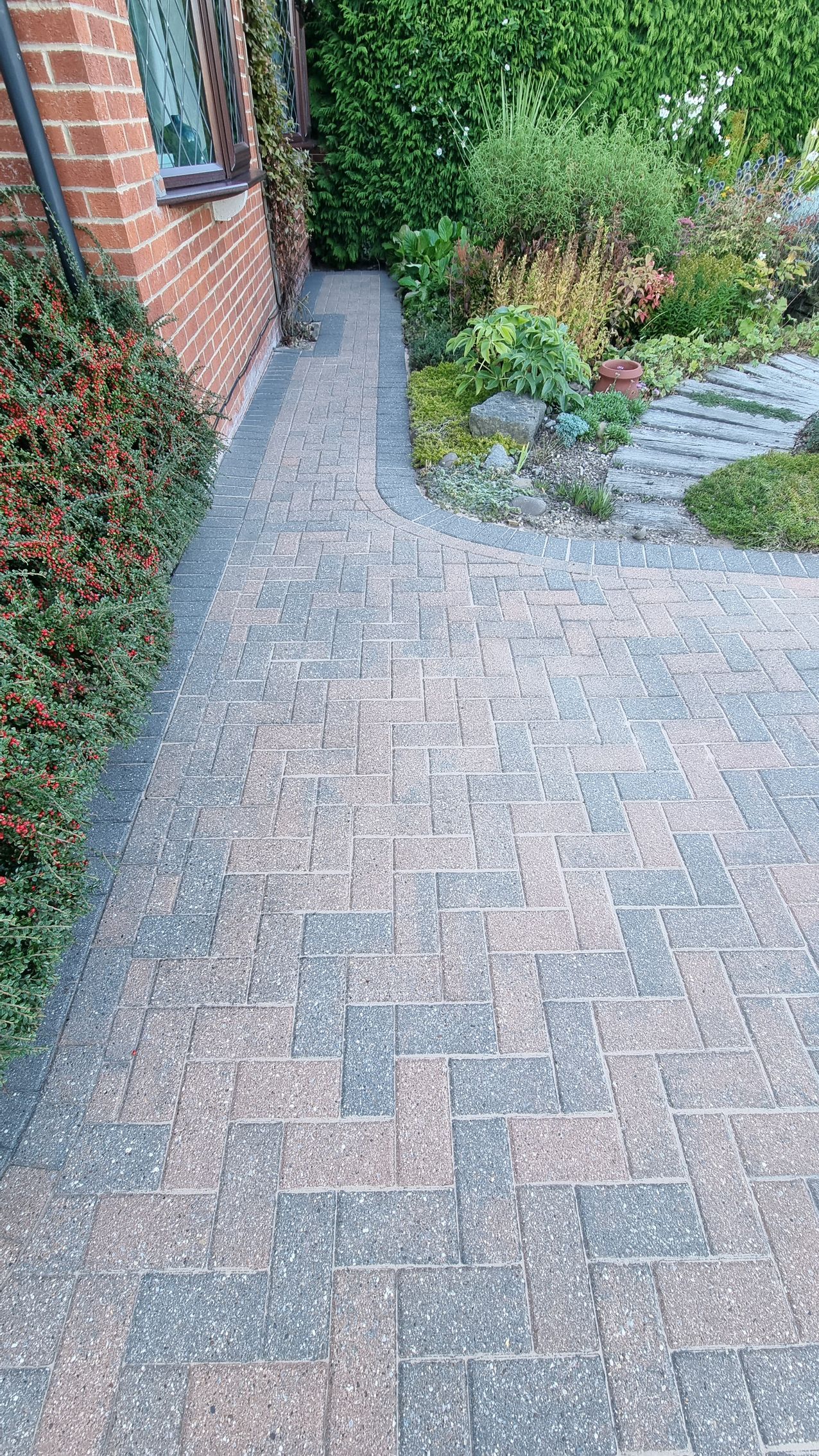 A block paved driveway in front of a brick house after being pressure washed by benchmark property services.