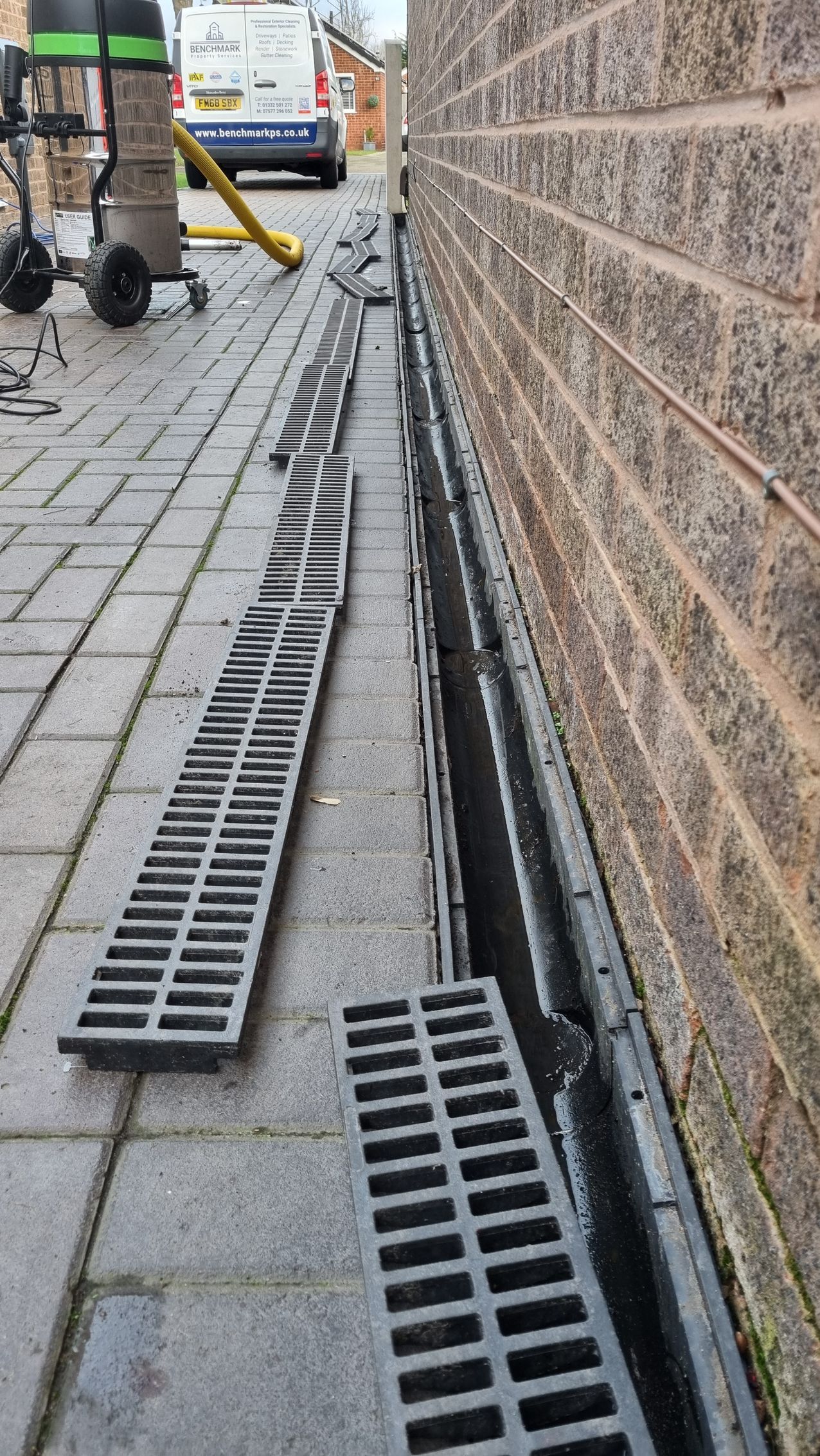 An ACO drain on the driveway next to a brick wall.