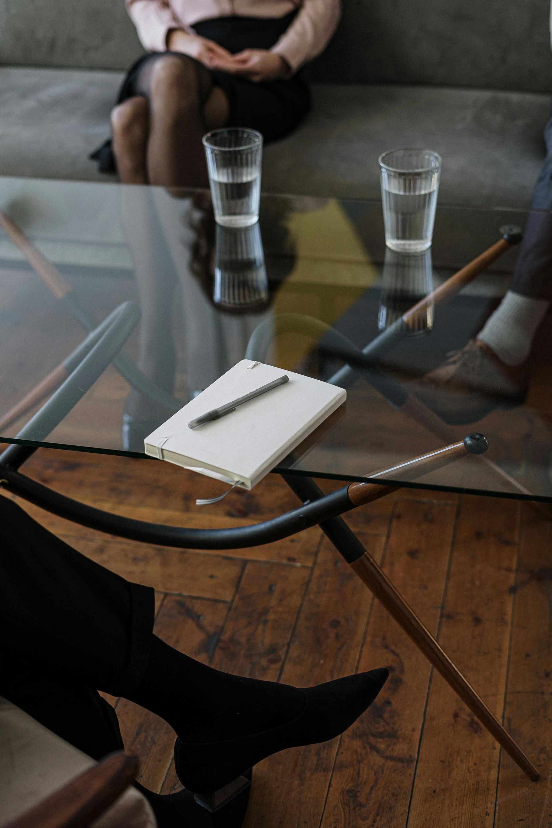 Des gens assis autour d'une table en verre avec des verres d'eau et un bloc-notes. Parquet.