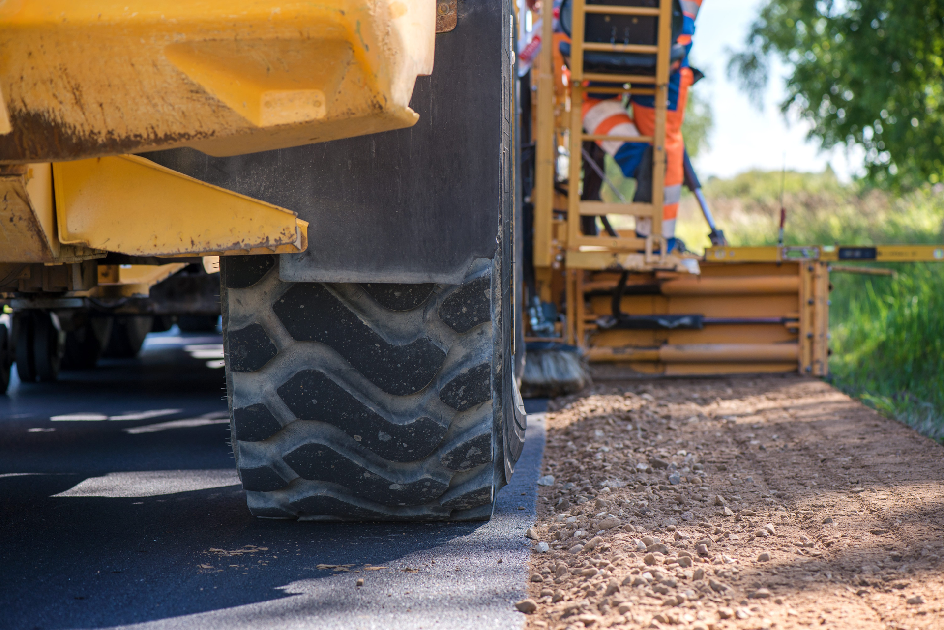 Road paver laying asphalt beside a large machine wheel on a road shoulder