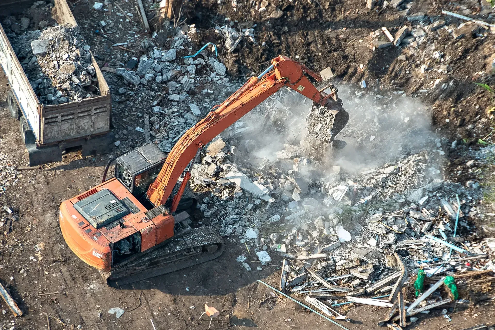 Orange excavator clearing debris in a smoky demolition site