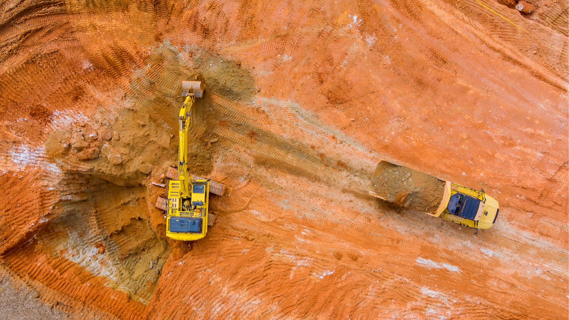 Yellow excavator and dump truck working on an orange dirt construction site.