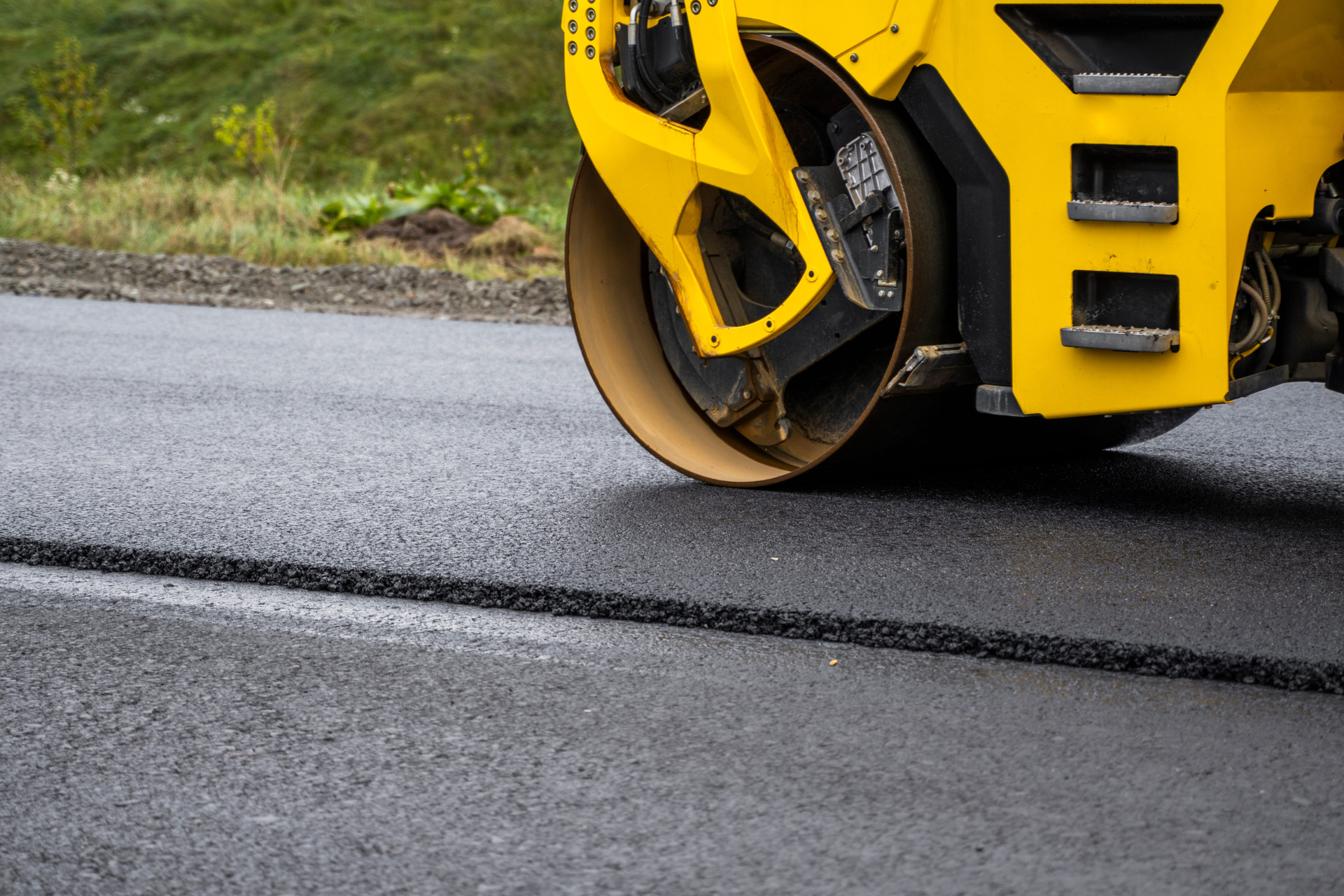 Yellow road roller compacting wet asphalt on a road
