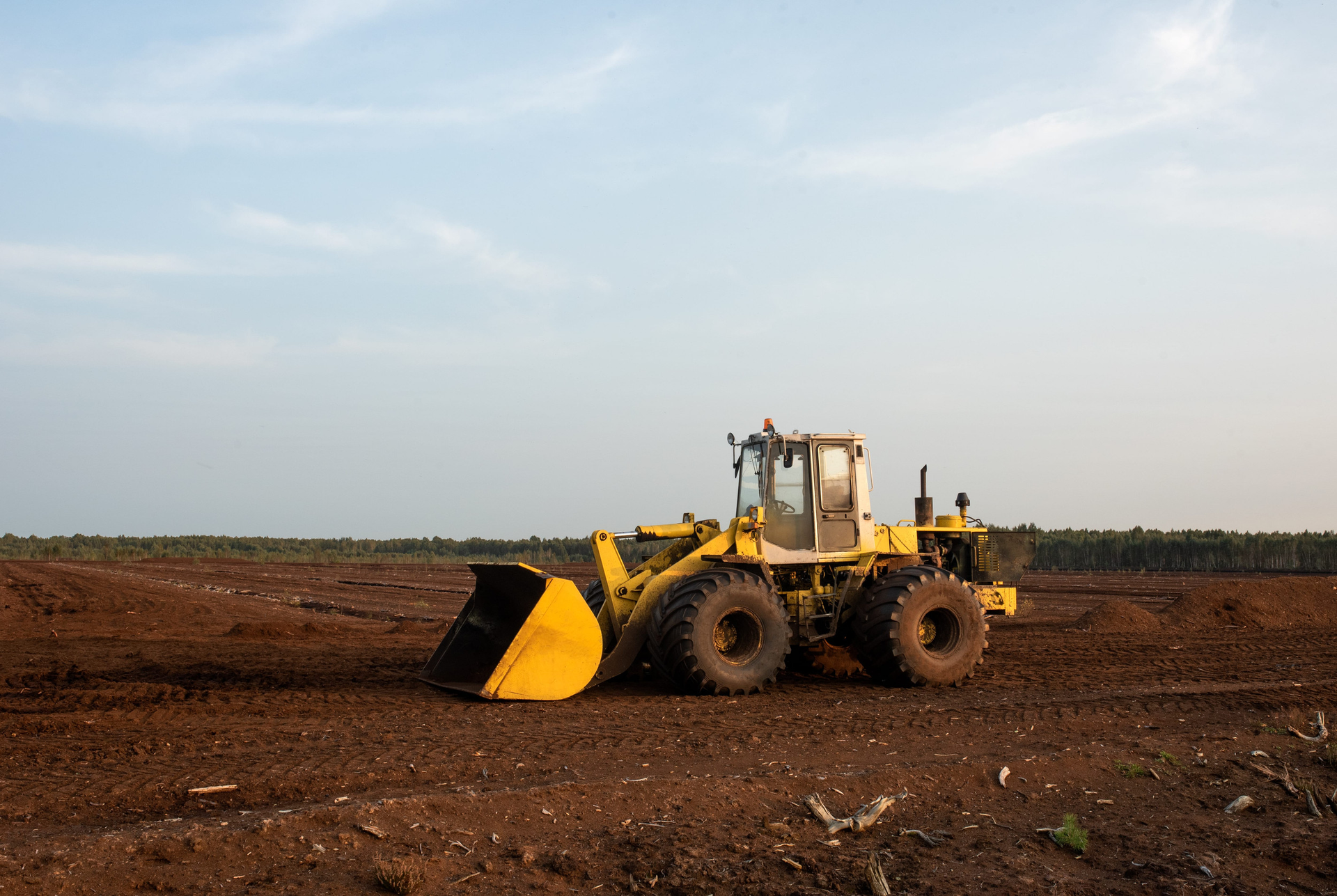 Yellow bulldozer on a dirt field under a cloudy sky
