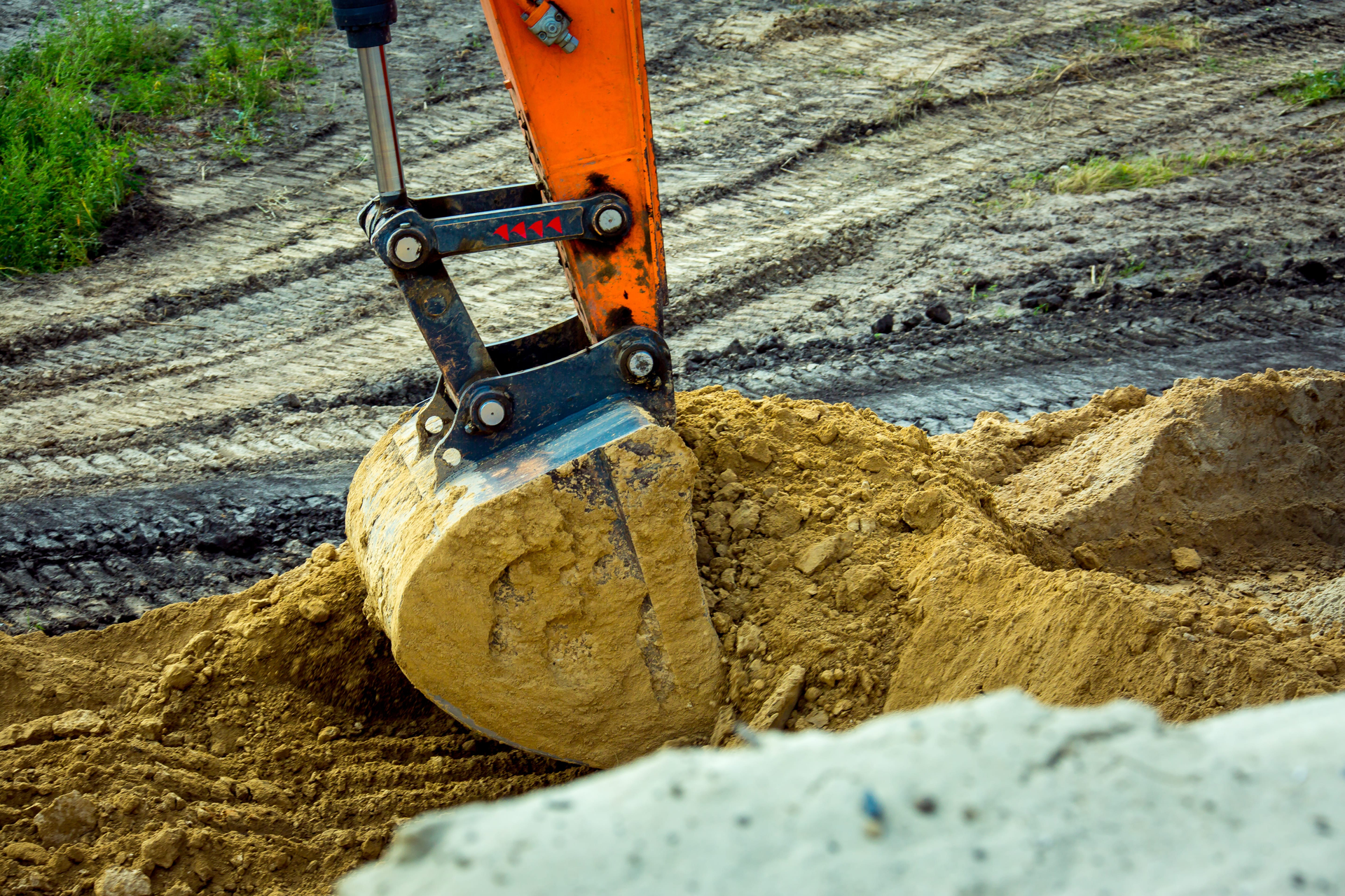 Excavator bucket digging into a sandy mound at a construction site