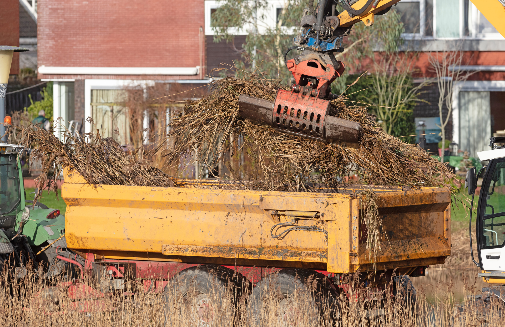 Orange truck with crane loading brush and branches near houses