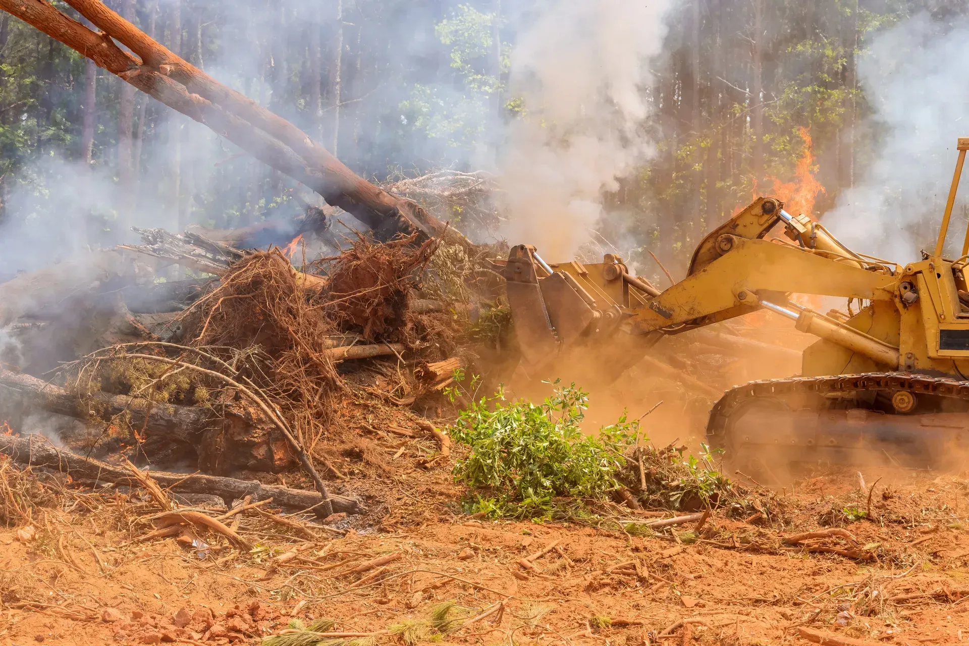 Bulldozer clearing a smoky pile of debris in a dusty outdoor site