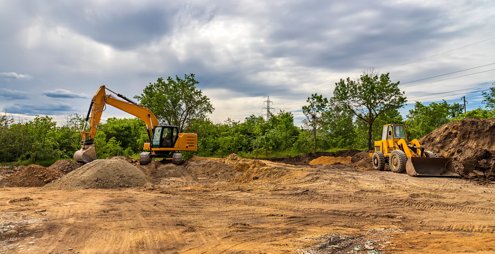 Excavator and loader working on a dirt construction site under a cloudy sky
