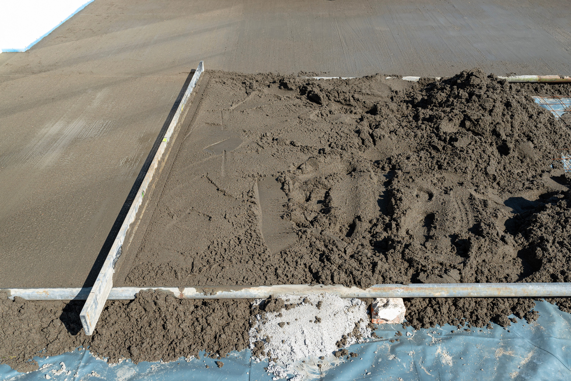 Fresh concrete slab with wooden forms, one section covered in dirt on a construction site
