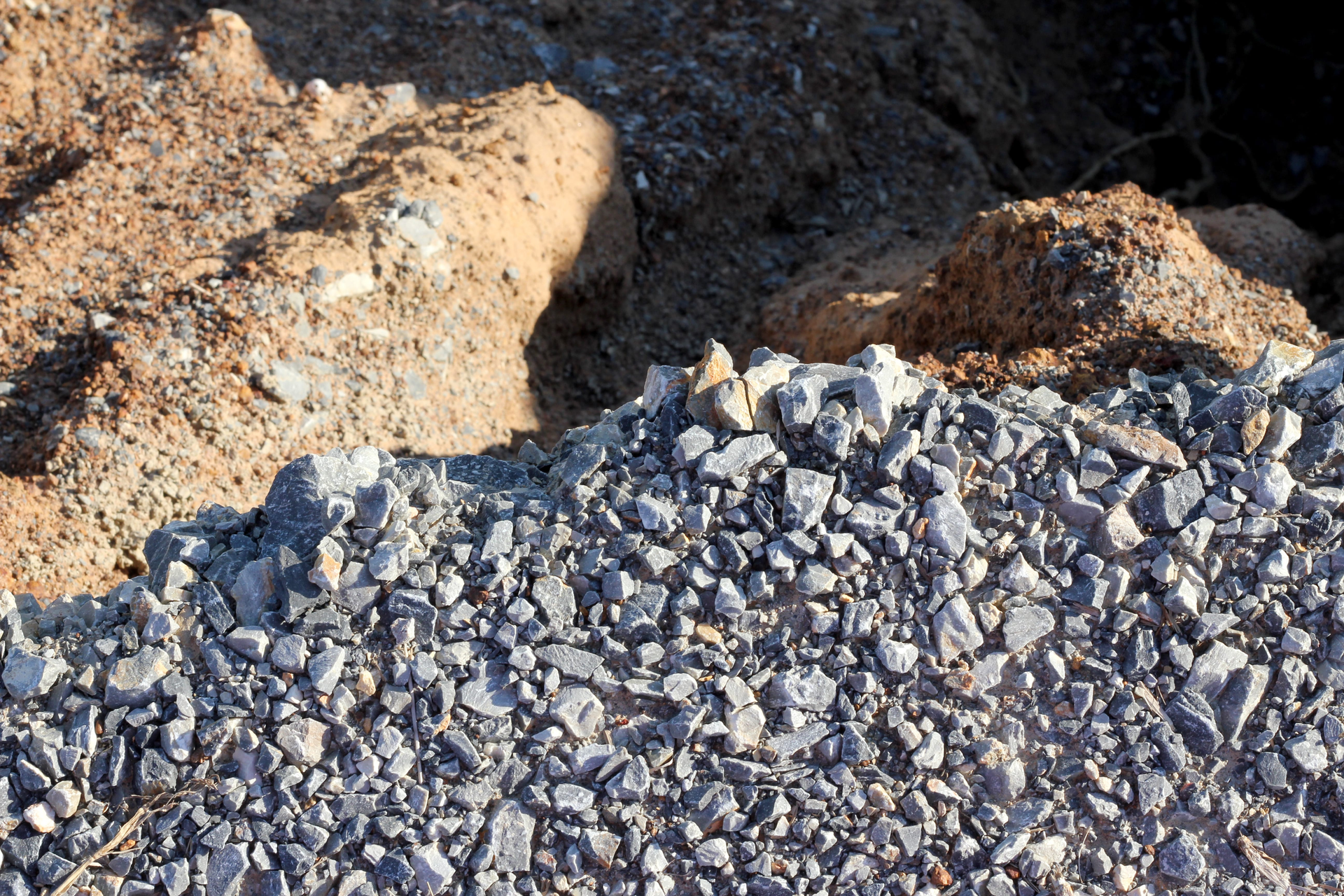 Pile of gray gravel in front of tan dirt mounds outdoors
