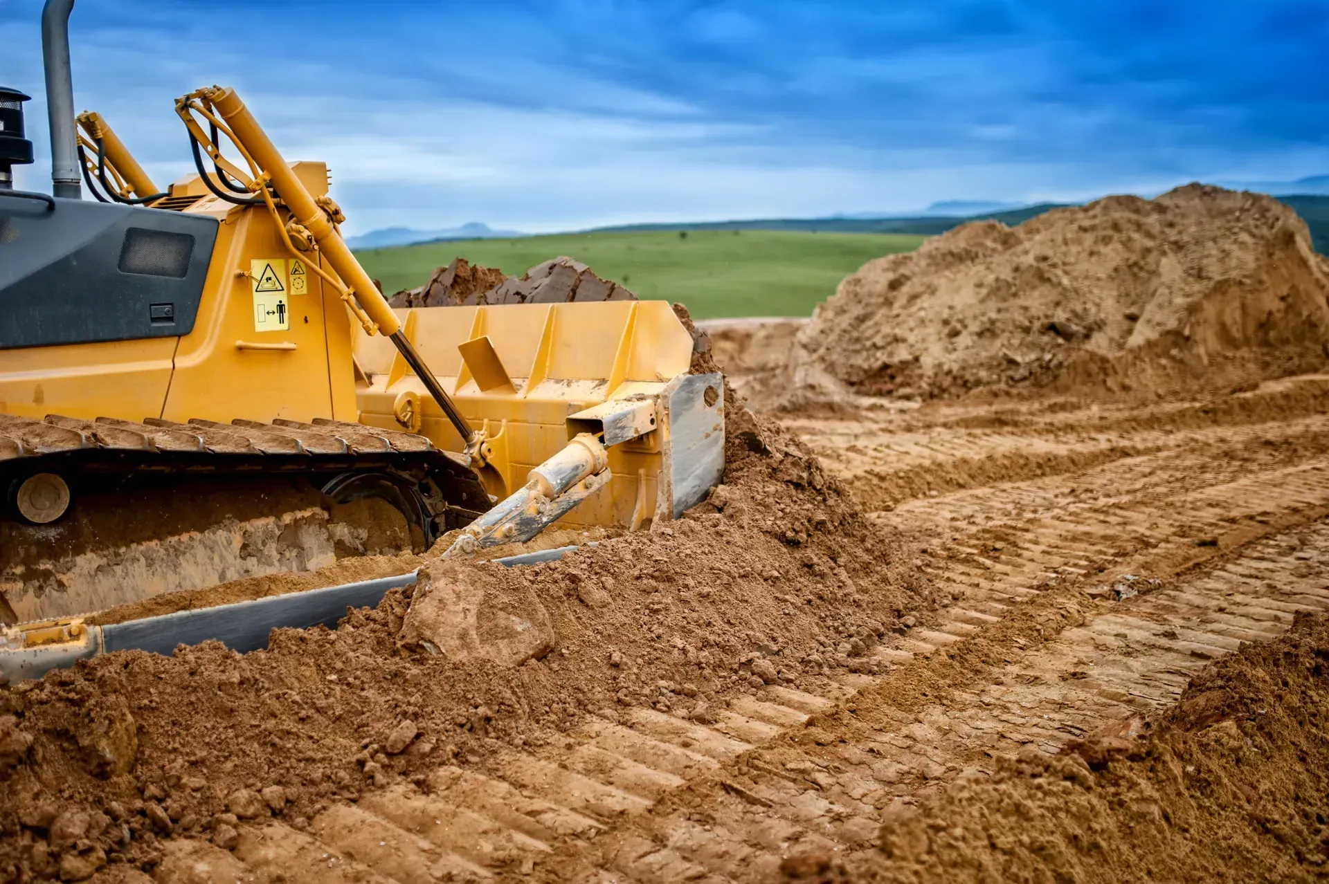 Yellow bulldozer pushing dirt at a construction site with piles of earth under a cloudy sky